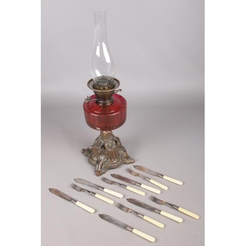 131 - A Victorian cranberry glass oil lamp along with a collection of fish knives and forks.