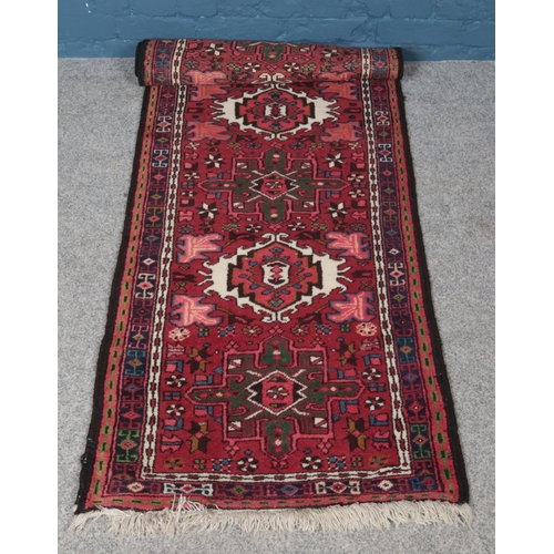 335 - A Persian red ground wool runner. With a geometric pattern within a border. L:209cm W:70cm.