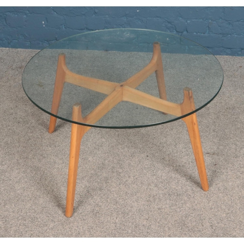 557 - A retro coffee table with wooden legs and circular glass top.