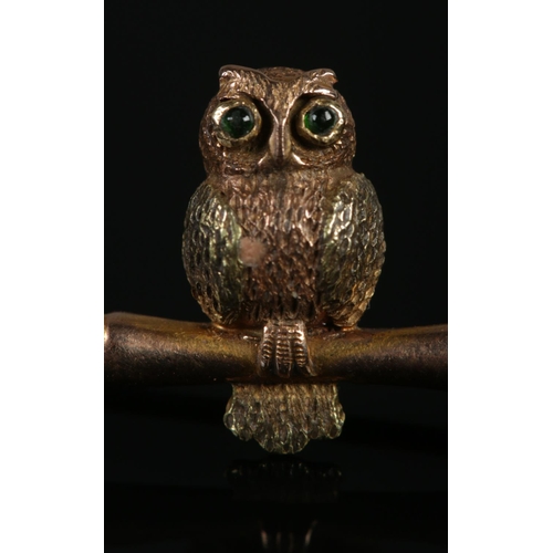 125 - A 9ct gold brooch formed as an owl perched on a branch, its eyes set with emerald coloured stones. 2... 