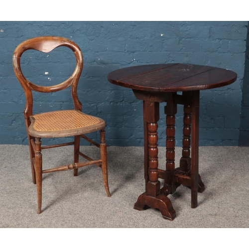 573 - An oak drop leaf table with turned supports together with a bergère base balloon back chair.