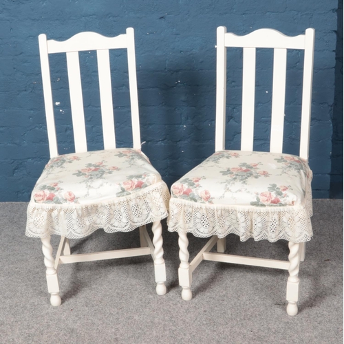 574 - A pair of white painted dining chairs with floral cushions.