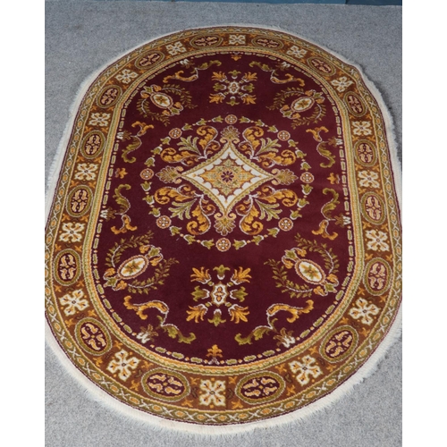 308 - A red ground oval rug with central medallion design. (200cm x 141cm)