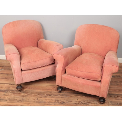 500 - A pair of Howard & Son style red upholstered armchairs raised on turned mahogany supports.