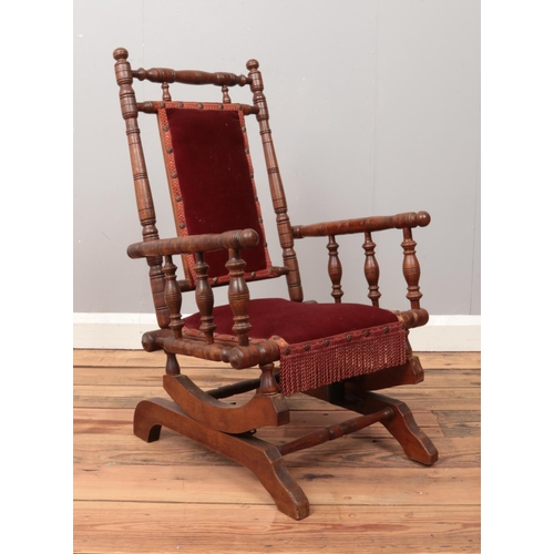 478 - A mahogany child's American rocking chair, with turned bobbin supports, in red fabric upholstery and... 