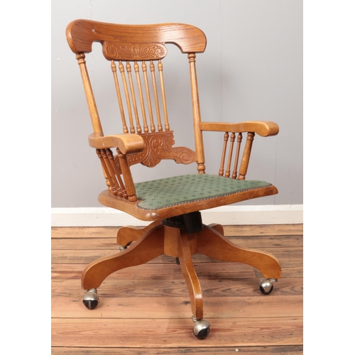 483 - A hardwood swiveling office armchair, with turned supports to back and arms, raised on casters.