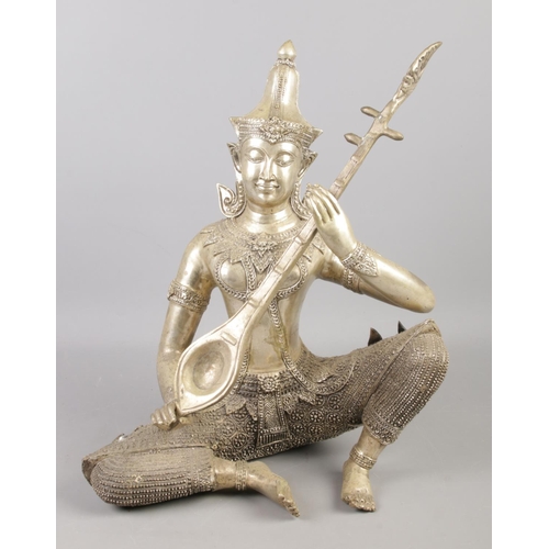 214 - A large Thai white metal sculpture of a seated deity playing a sitar. 40cm.