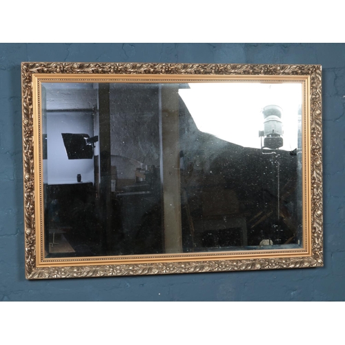 423 - A gilt framed bevel edge mirror featuring floral decoration. Approx. dimensions 96.5cm x 67cm.