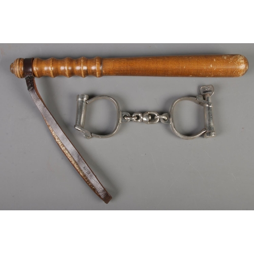 30 - A turned wood truncheon (40cm) along with a pair of antique police handcuffs with key.