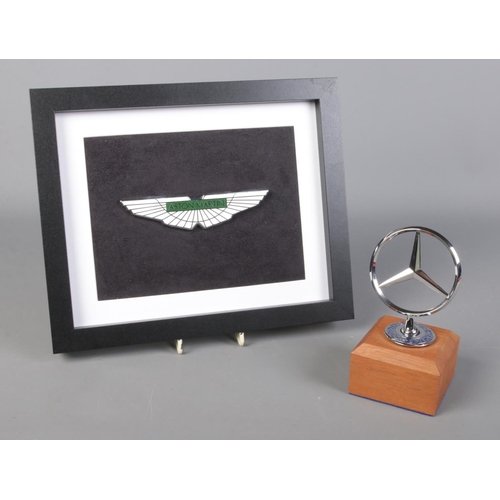 233 - A framed enamel Aston Martin badge, together with a mounted Mercedes Benz three pointed star.