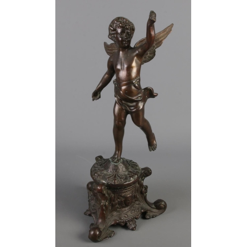 129 - A bronze figure formed as a cherub. Raised on ornate base with mask decoration. (48cm)