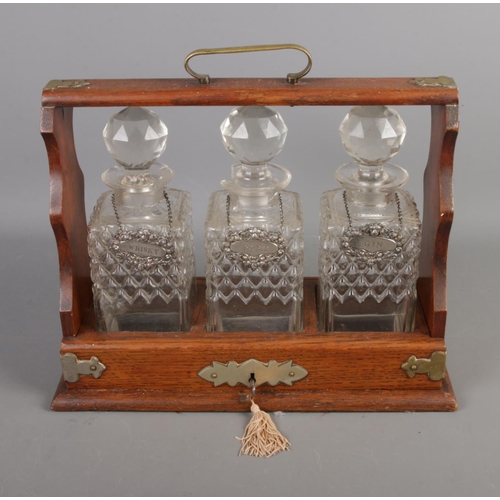 102 - A three decanter tantalus with key featuring silver plated labels with Lion head decoration.