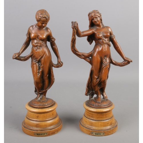 43 - A pair of cast metal figures raised on wooden plinths, titled Modistie and Gaiete. 30cm.