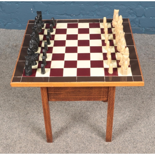 593 - A tile topped chess table containing carved pieces. Chess set is complete.