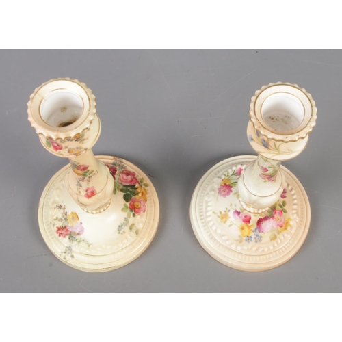 400 - Two Royal Worcester blushware candlesticks on circular bases, decorated with flowers. Dated 1900 and... 