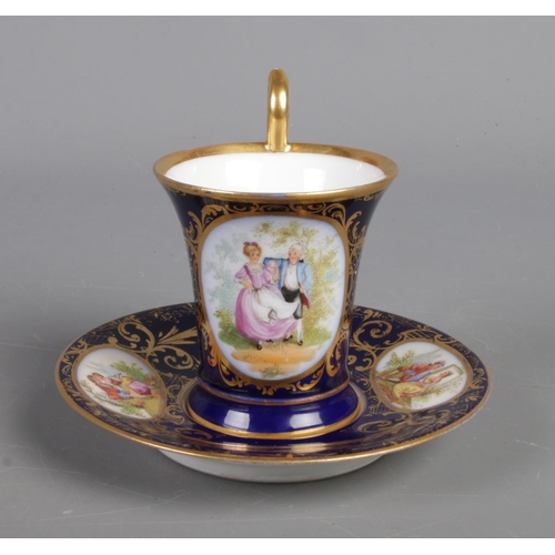 402 - A twentieth century porcelain cup and saucer, with blue and gilt design and hand-painted panels depi... 