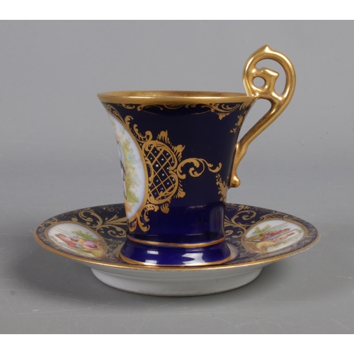 402 - A twentieth century porcelain cup and saucer, with blue and gilt design and hand-painted panels depi... 