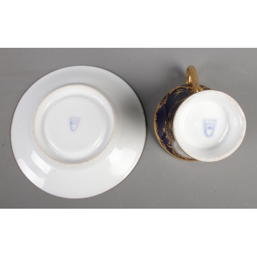 402 - A twentieth century porcelain cup and saucer, with blue and gilt design and hand-painted panels depi... 