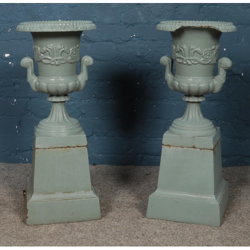 301 - A pair of painted cast iron twin handled garden urns, raised on square bases. Height: 69cm.