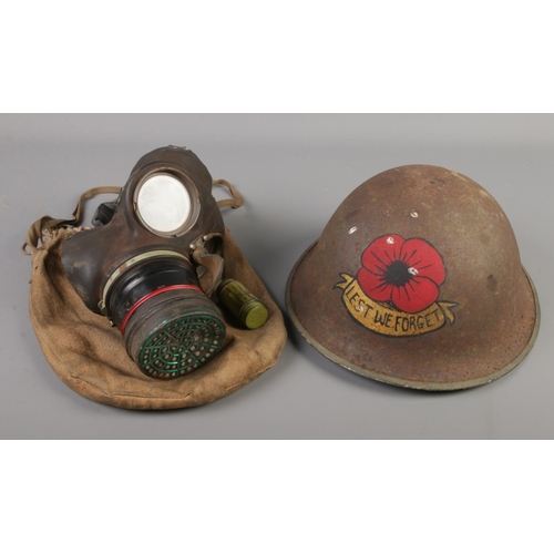 83 - A WWII gas mask along with a tommy helmet with painted Lest We Forget rose.