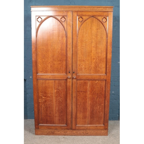 460 - An oak double wardrobe, with arched panels and clover detailing. Height: 182cm, Width: 112cm, Depth:... 