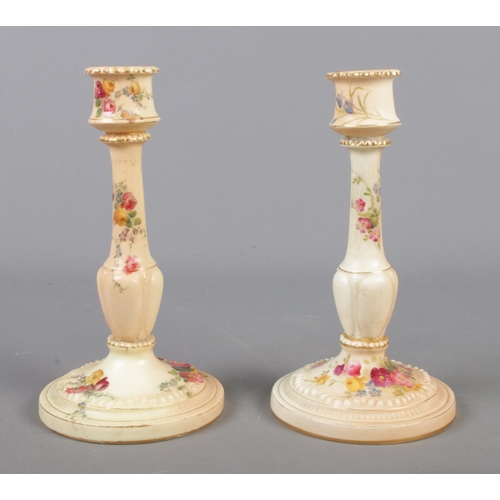 414 - Two Royal Worcester blushware candlesticks on circular bases, decorated with flowers. Dated 1900 and... 