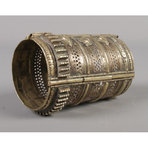 24 - An eastern brass bangle with pierced detailing. 10.5cm long.