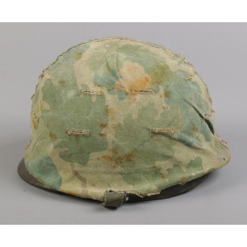 100 - A vintage military helmet with camouflage cover and 
 broad arrow mark to inside; stamped 21 July 19... 