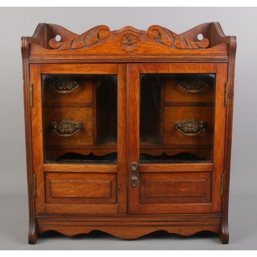 105 - An oak smokers cabinet with carved pediment and beveled glass doors. 46cm high.