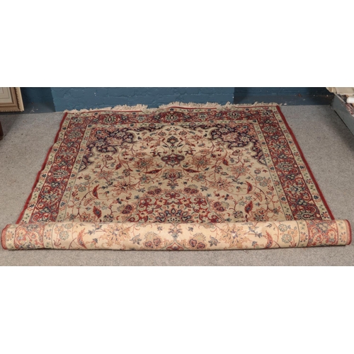 250 - A large ground wool rug featuring red and cream floral pattern and fringe trim.