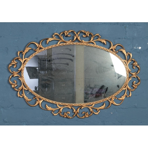 362 - A gilt scroll framed elliptical mirror. Approx. dimensions 83cm x 54cm.