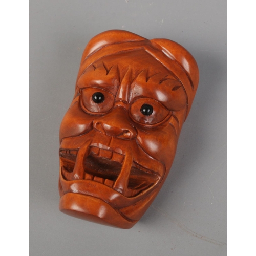 397 - A Japanese carved Netsuke in the form of a Oni mask. Signed. Approx. length 5.5cm.