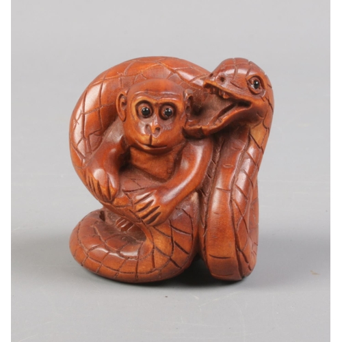 401 - A Japanese carved Netsuke in the form of a monkey wrapped by a snake. Signed. Approx. height 4cm.