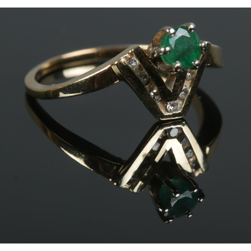 423 - A modern emerald ring, set into a chevron of channel set small diamond. Tests to 14ct Gold. Size O. ... 