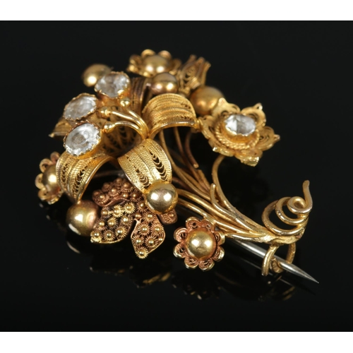 115 - An 18ct gold cannetille work flower brooch set with four paste stones. Maker's mark FM. 4.5cm x 3.5c... 