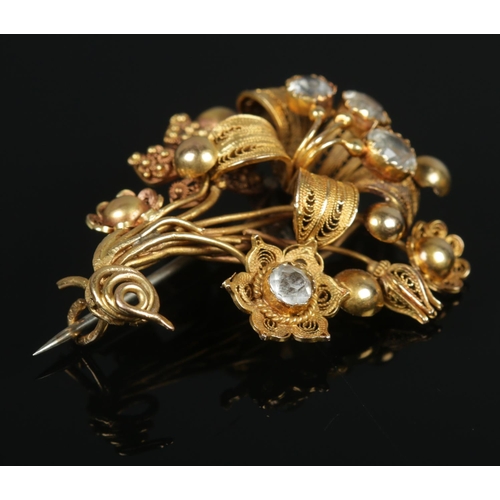 115 - An 18ct gold cannetille work flower brooch set with four paste stones. Maker's mark FM. 4.5cm x 3.5c... 