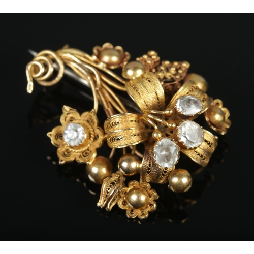 115 - An 18ct gold cannetille work flower brooch set with four paste stones. Maker's mark FM. 4.5cm x 3.5c... 