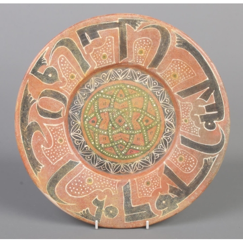 14 - An Islamic Samanid style earthenware dish with Kufic border and central motif. Diameter 32.5cm.