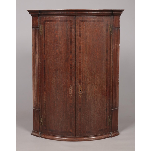 175 - A large Georgian oak bow front corner cupboard with crossbanded doors. With key. Height 96cm, Depth ... 