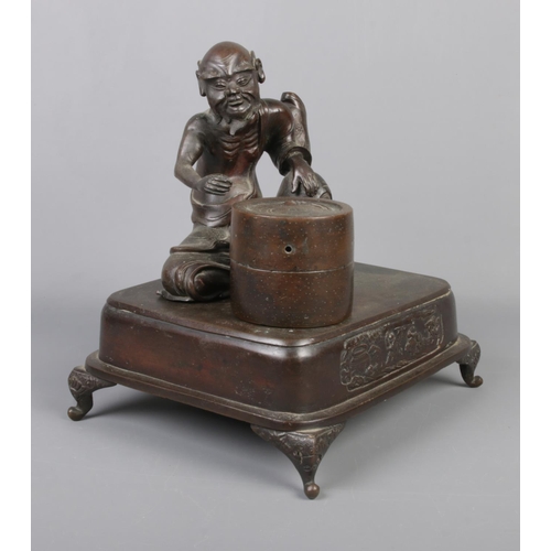 9 - A Japanese bronze desk stand formed as a seated man and a barrel raised on square plinth with scroll... 