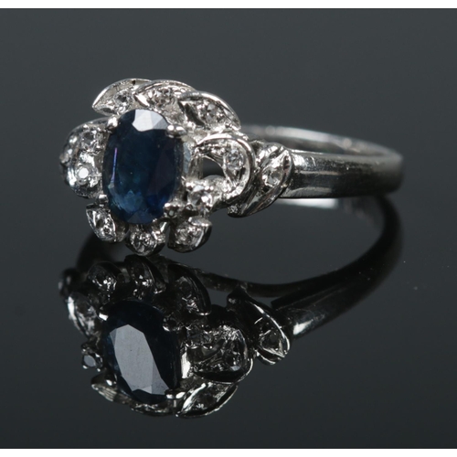 514 - A rhodium plated silver ring set with a central sapphire surrounded by white paste stones. Size M 1/... 