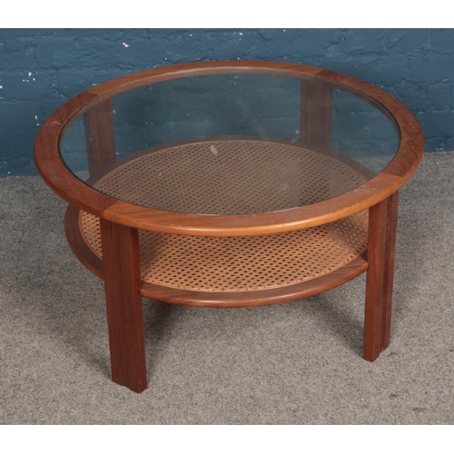 557 - A teak circular glass top coffee table featuring bergere under tier. Approx. diameter 82cm.