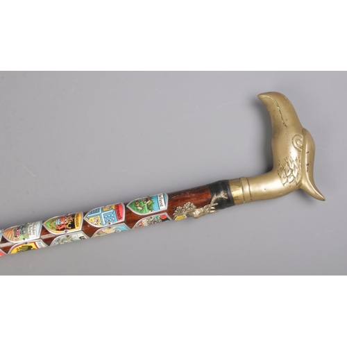 169 - A brass handled walking stick formed as a bird's head. Decorated with souvenir shields from various ... 