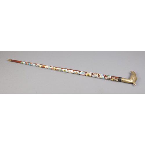 169 - A brass handled walking stick formed as a bird's head. Decorated with souvenir shields from various ... 