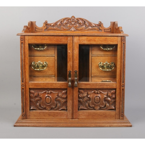 6 - An oak smokers cabinet featuring carved detailing to doors and pediment and beveled glass panels. Wi... 