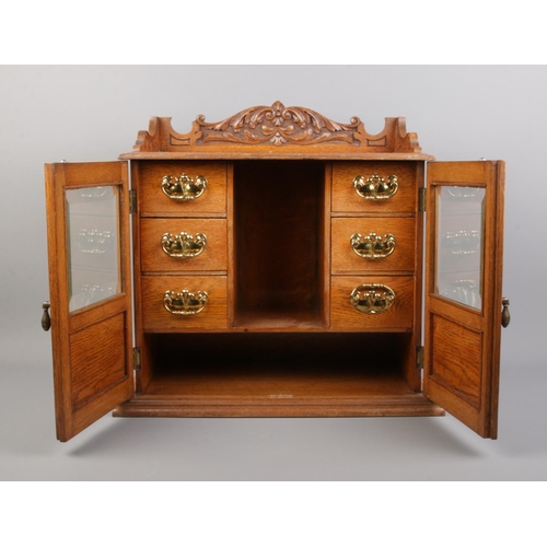 6 - An oak smokers cabinet featuring carved detailing to doors and pediment and beveled glass panels. Wi... 