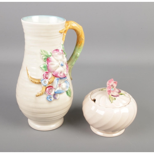 419 - Two pieces of Clarice Cliff pottery. Includes floral decorated handled vase and preserve pot.