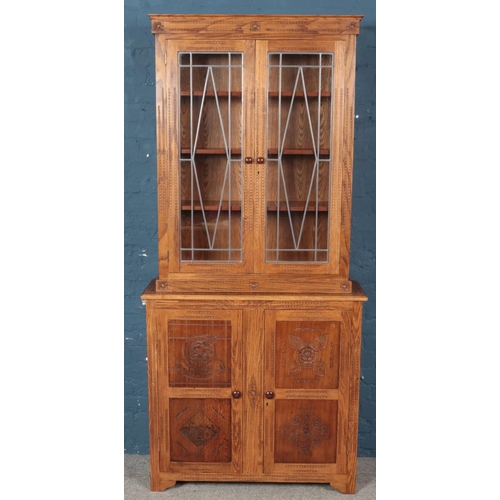 443 - A carved oak lead glazed bookcase with cupboard base. With panelled doors carved with four individua... 