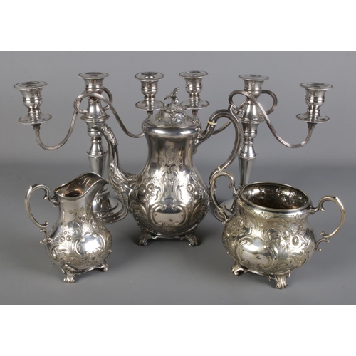 73 - A ornate silver plate three piece teaset along with a pair of silver plate candelabra.