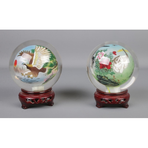 64 - A pair of oriental reverse hand painted spherical glass ornaments depicting eagles and cats, on carv... 